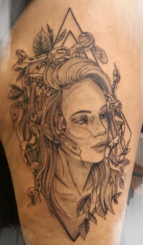 Black-and-grey tattoo of a Medusa with snakes winding through her hair inside a thin diamond frame on a thigh