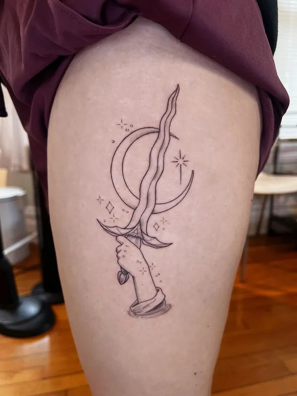 Fine-line tattoo of a hand holding a twisted dagger in front of a crescent moon with sparkles on a thigh