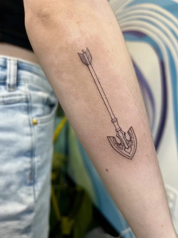 Fine-line tattoo of a slender arrow with a trident-shaped arrowhead marked with a small heart on a forearm