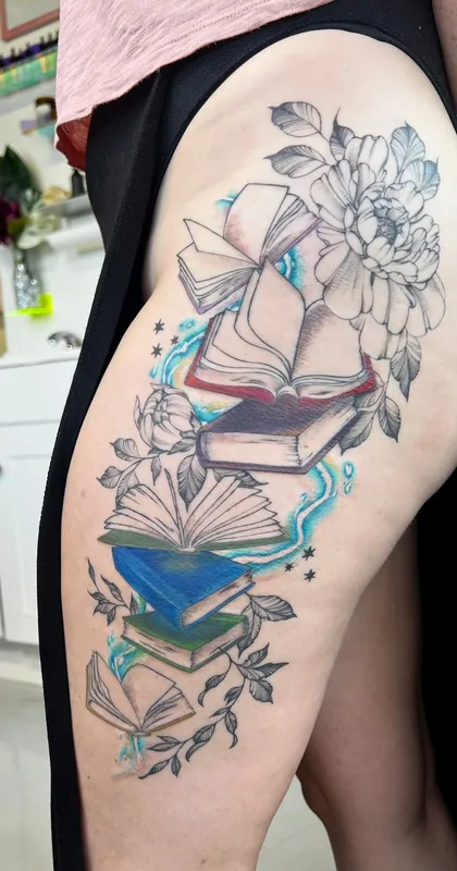 Tattoo of a tumbling stack of open and closed books with teal color glow and peonies running down a hip and thigh
