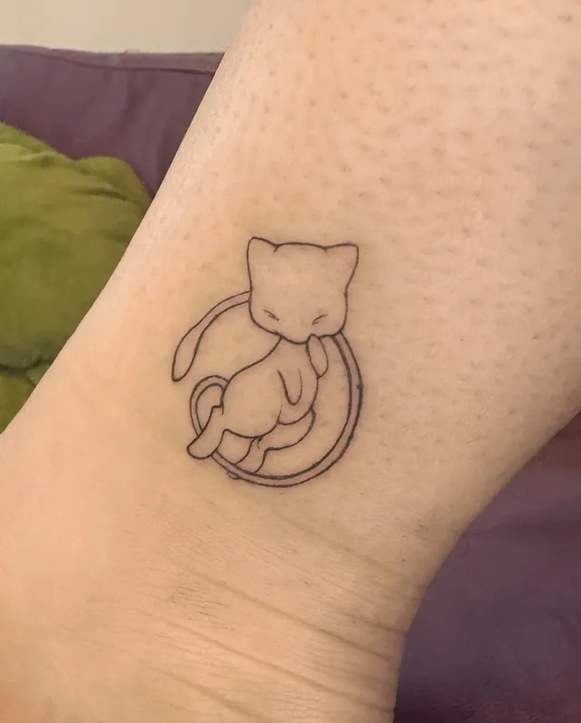 Minimal fine-line tattoo of Mew from Pokemon curled asleep inside a thin circle above an ankle