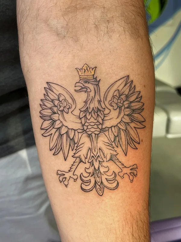 Fine-line tattoo of the crowned Polish white eagle coat of arms with a gold color crown on a forearm