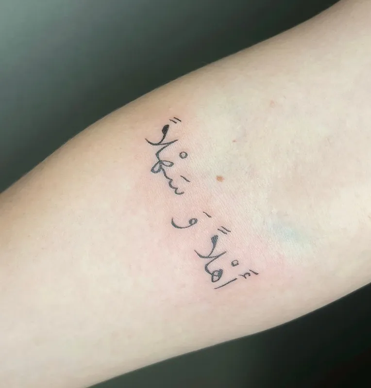 Fine-line Arabic script tattoo in two short lines of calligraphy on an inner forearm