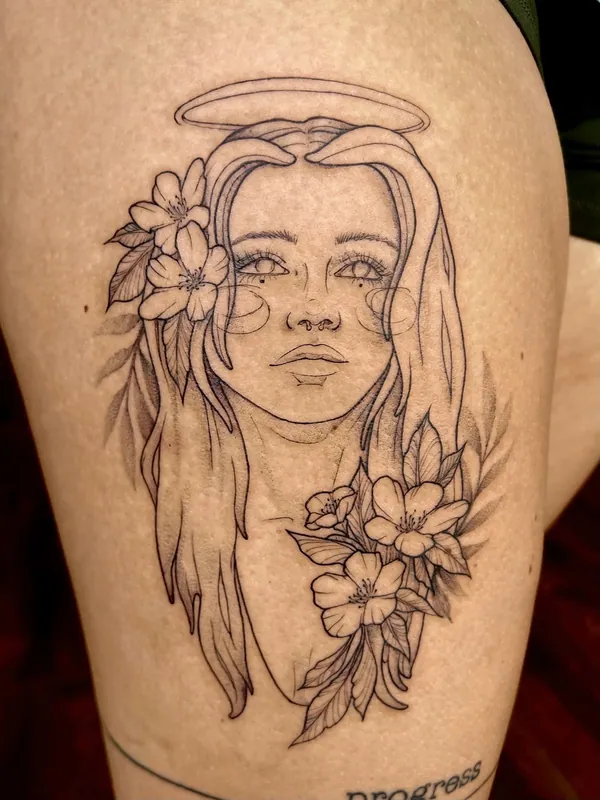 Fine-line black-and-grey tattoo of a haloed woman's face with blossoms in her hair and at her collar on a thigh