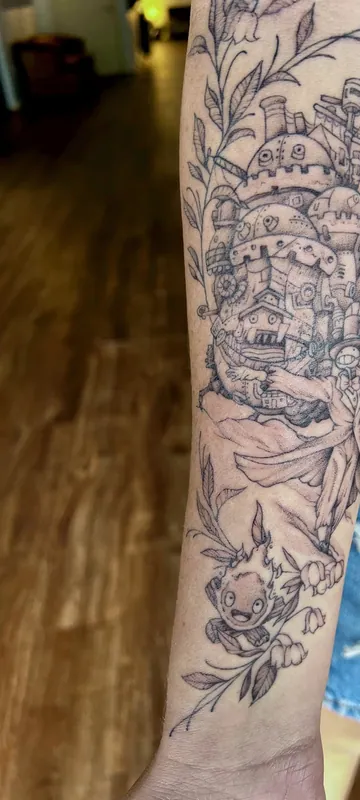Black-and-grey Studio Ghibli sleeve tattoo of Howl's Moving Castle with Calcifer and trailing botanicals down a forearm