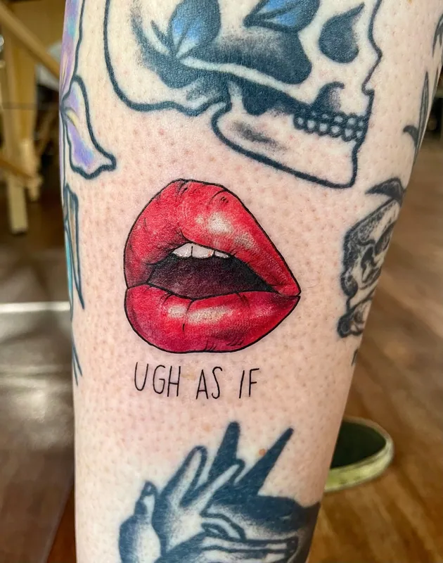 Color tattoo of glossy red lips above the lettering 'ugh as if' among older tattoos