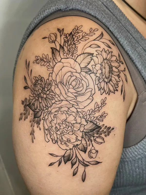 Black-and-grey fine-line floral bouquet tattoo with a rose, peony, sunflower and chrysanthemum on a shoulder