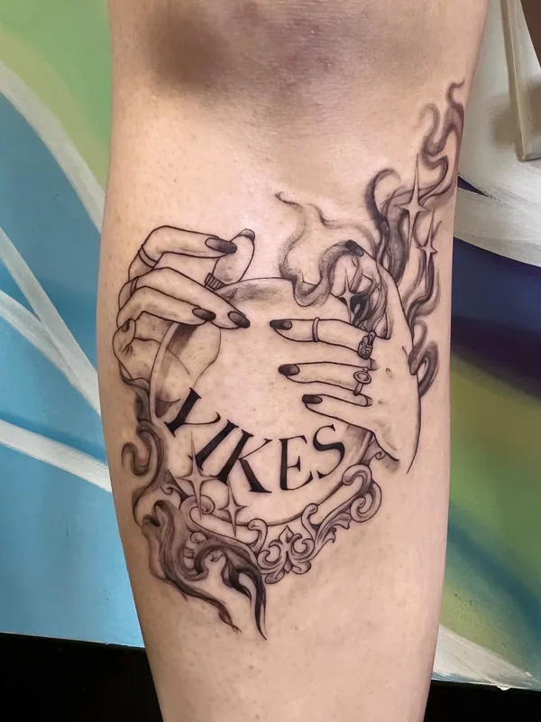 Black-and-grey tattoo of two hands over a crystal ball with smoke, sparkles and the word 'Yikes' in an ornate frame on a calf