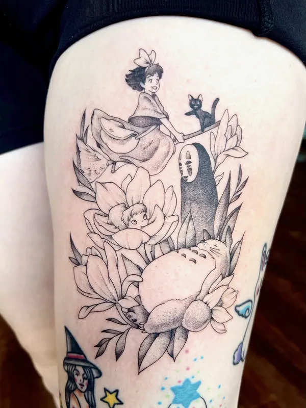 Black-and-grey Studio Ghibli tattoo with Kiki on her broom, Jiji, No-Face and Totoro among magnolia blooms on a thigh