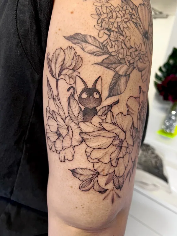 Fine-line black-and-grey tattoo of a black cat peeking from irises and lilac blooms on an upper arm
