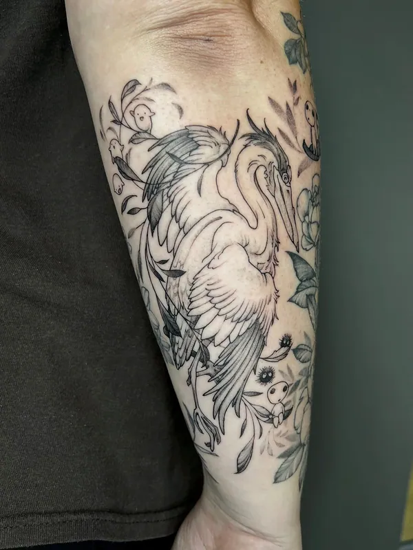 Black-and-grey fine-line tattoo of a heron with wings spread among blossoms and small kodama spirits on a forearm