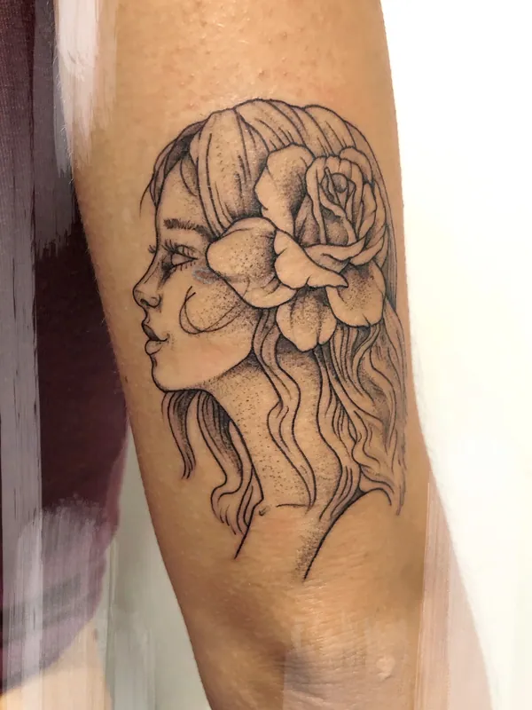 Fine-line black-and-grey tattoo of a woman in profile with a rose tucked into her hair on a forearm