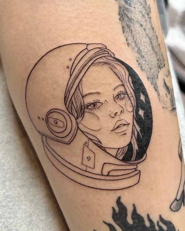 Fine-line tattoo of a woman's face inside an astronaut helmet with stars on an upper arm