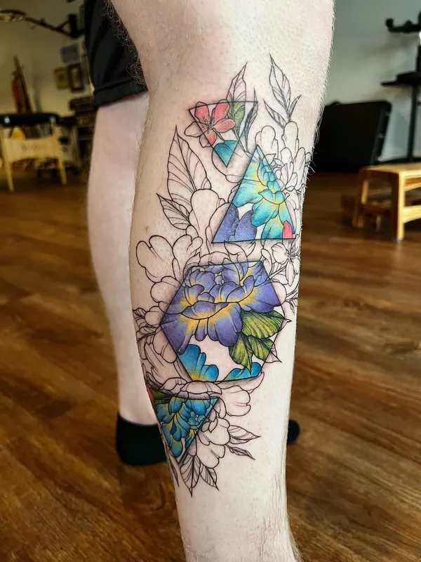 Tattoo of peonies drawn in fine line that fill with blue and green color inside stacked geometric triangles on a calf
