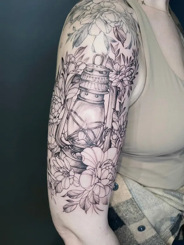 Black-and-grey half-sleeve tattoo of an oil lantern surrounded by peonies and chrysanthemums on an upper arm