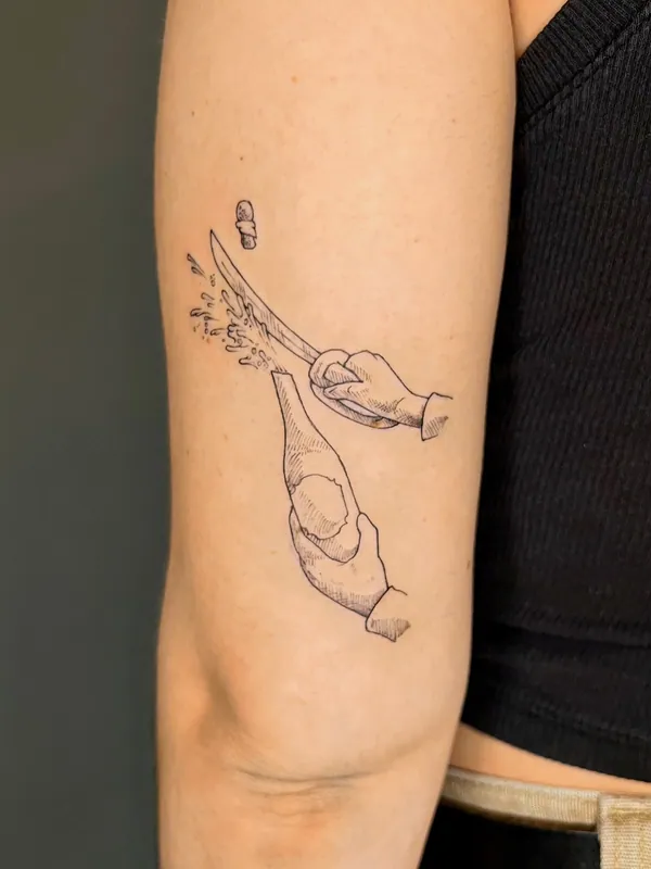 Fine-line black-and-grey tattoo of two hands sabering a champagne bottle, cork flying, on an upper arm