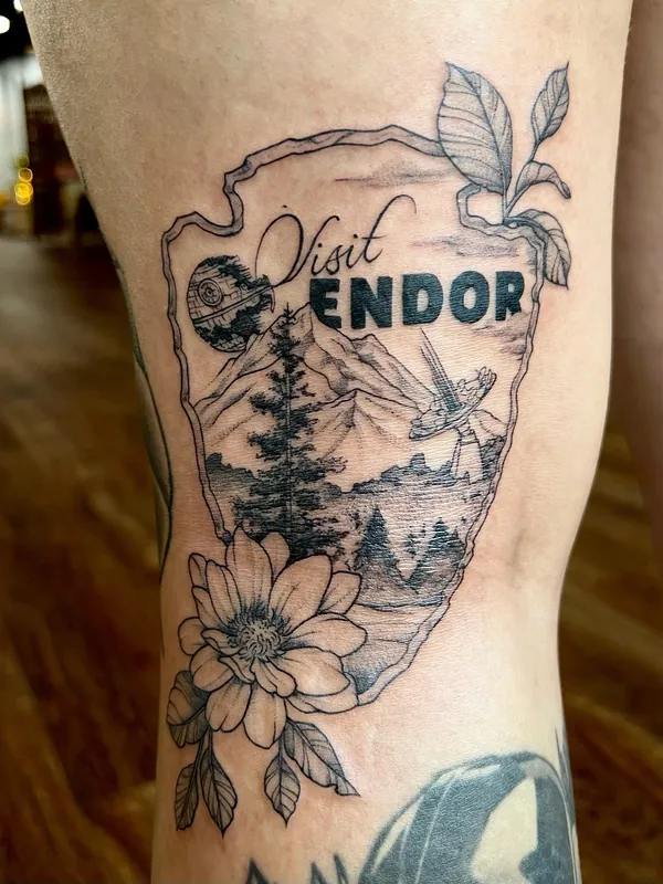 Black-and-grey 'Visit Endor' Star Wars tattoo styled as a park badge with the Death Star, an AT-ST and forest, on a thigh