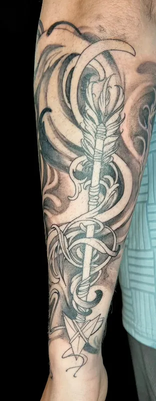 Black-and-grey ornamental arrow tattoo wrapped in flowing swirls running the length of a forearm