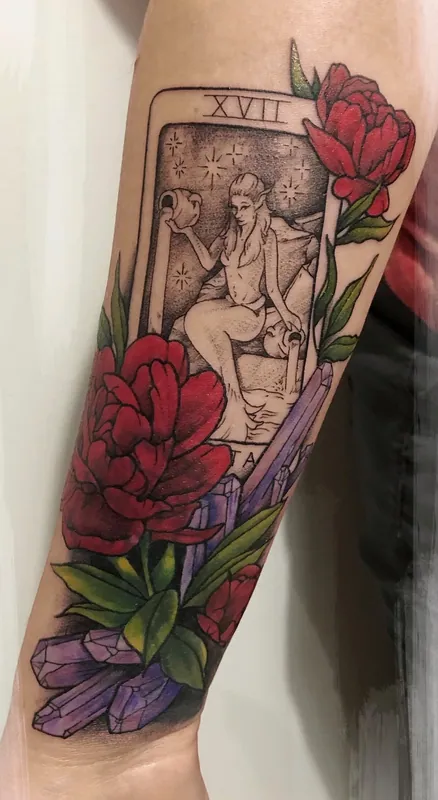 Tattoo of The Star tarot card in black-and-grey with red color peonies and purple crystals on a forearm