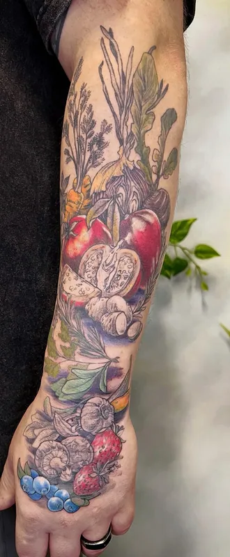 Color botanical sleeve tattoo of beets, figs, mushrooms, garlic, herbs, strawberries and blueberries running from forearm onto the hand