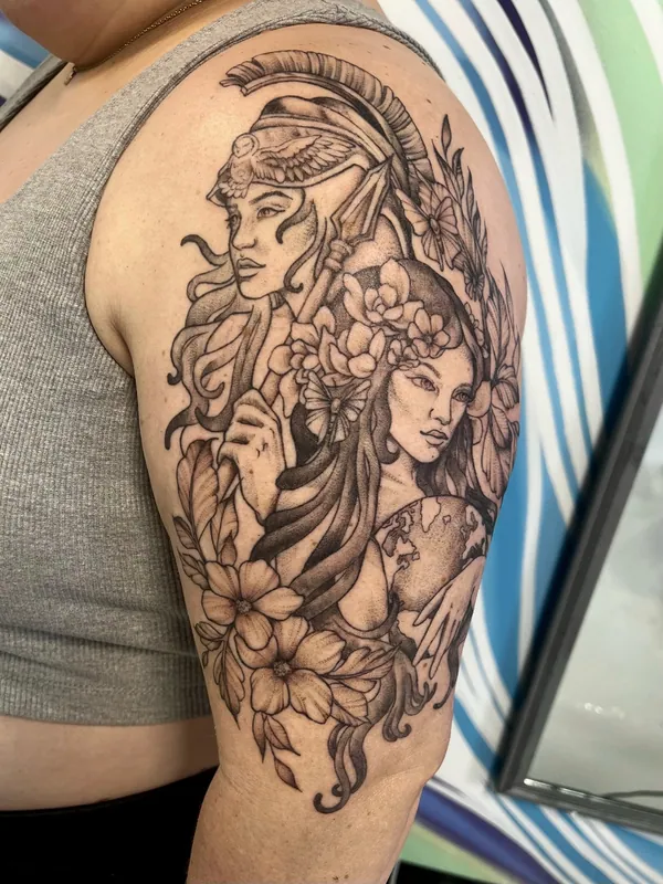 Black-and-grey tattoo of a helmeted Athena with a spear beside a flower-crowned woman holding a globe on an upper arm