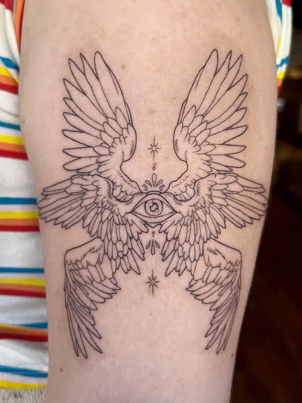 Fine-line seraphim tattoo of six wings around an all-seeing eye with small stars on an upper arm
