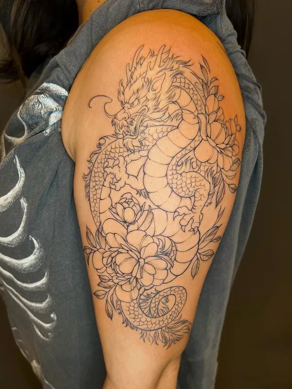 Linework tattoo of an eastern dragon coiling through peonies from the shoulder down an upper arm