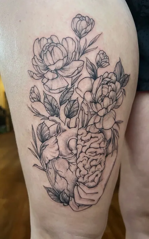 Fine-line black-and-grey tattoo of a hand holding a half-heart, half-brain with peonies growing from it on a thigh