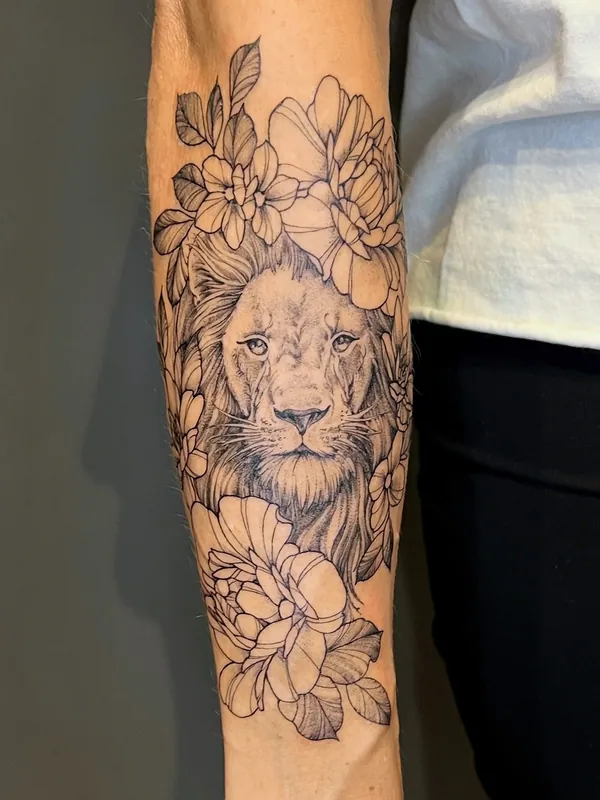 Black-and-grey fine-line lion portrait tattoo framed above and below by peonies and leaves on a forearm
