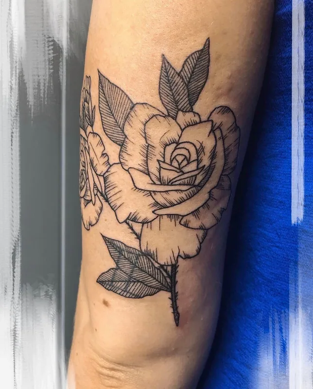 Linework rose tattoo with etched hatching on the leaves and petals on an upper arm