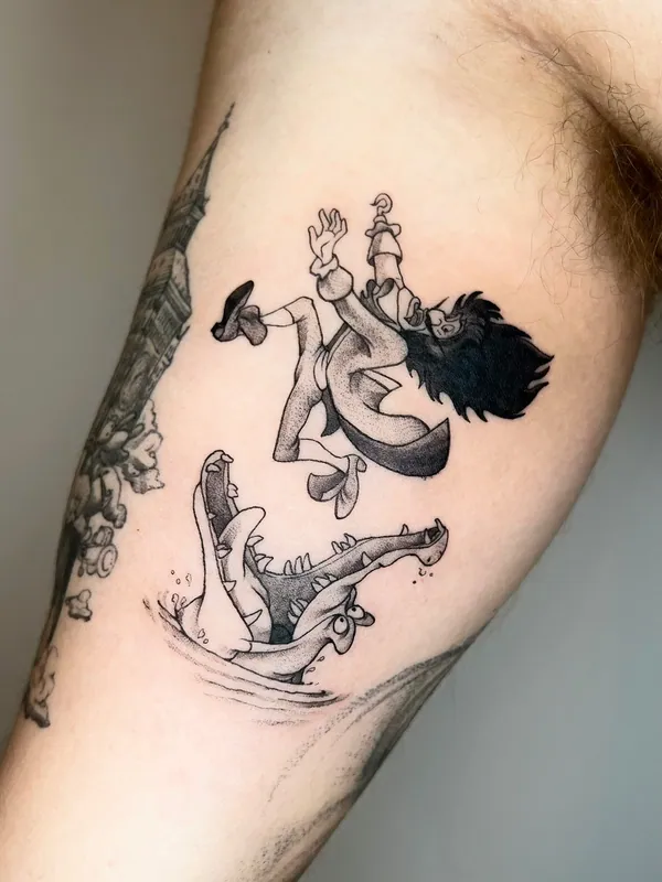 Black-and-grey tattoo of Captain Hook falling toward the crocodile from Peter Pan on an inner upper arm