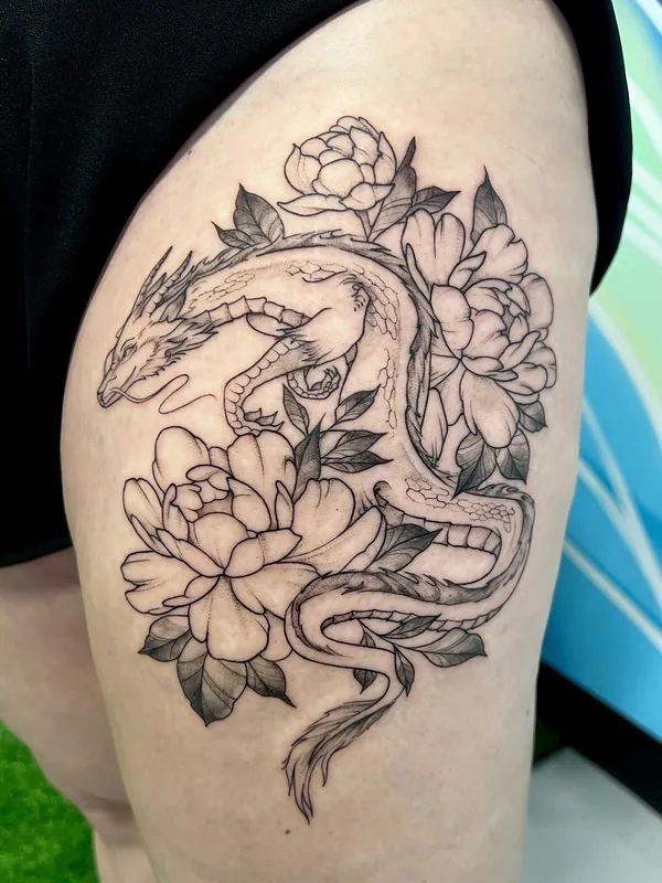 Fine-line black-and-grey eastern dragon tattoo winding through three peony blooms on a thigh