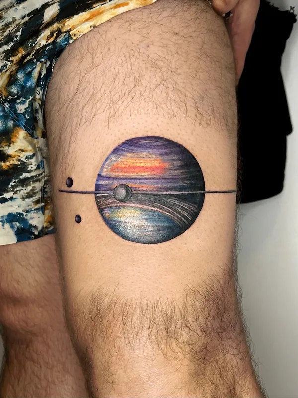 Color tattoo of a banded gas-giant planet bisected by a thin ring line with two small moons on a thigh