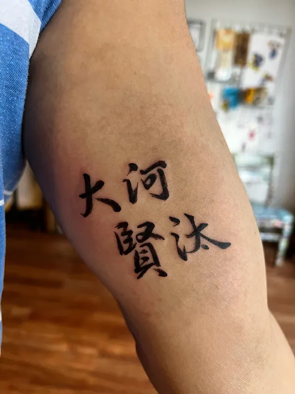 Brush-style Japanese kanji calligraphy tattoo in four characters on an inner upper arm