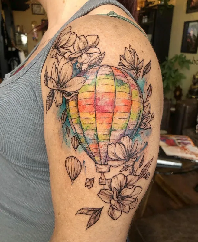 Healed color hot-air balloon tattoo with rainbow watercolor panels, two smaller balloons and magnolias on a shoulder