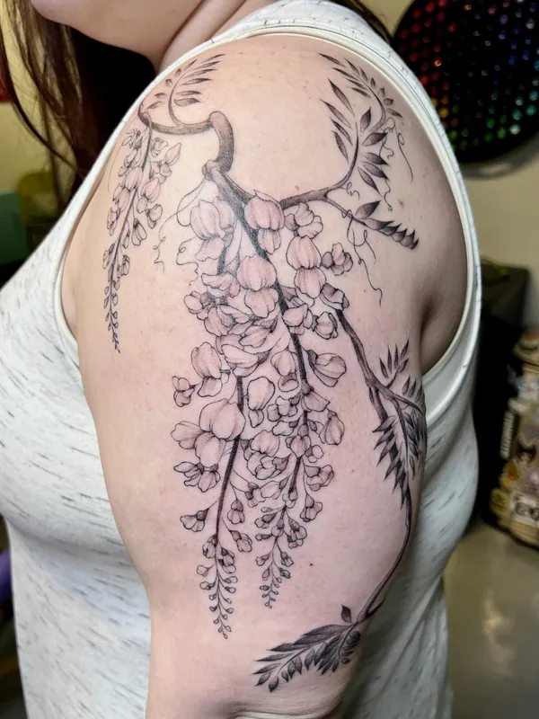 Black-and-grey fine-line wisteria tattoo cascading from the shoulder down an upper arm