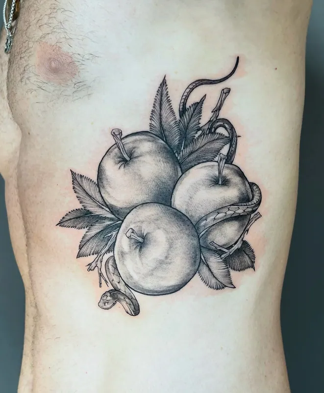 Black-and-grey tattoo of three apples with leaves and a snake winding between them on the ribs