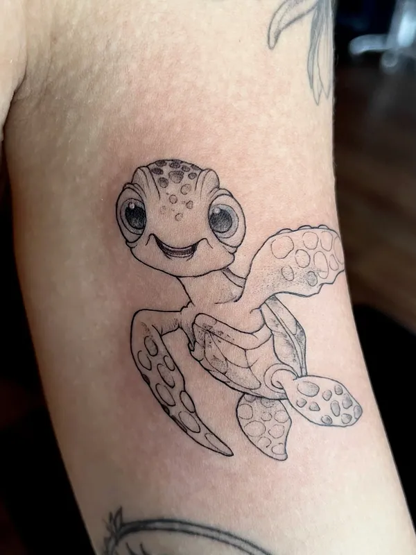 Fine-line black-and-grey tattoo of Squirt the baby sea turtle from Finding Nemo on an inner upper arm
