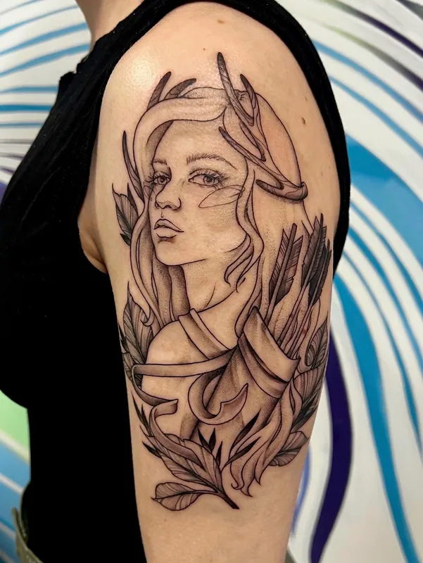 Black-and-grey tattoo of a woman with antlers, a quiver of arrows and feathers at her shoulders on an upper arm