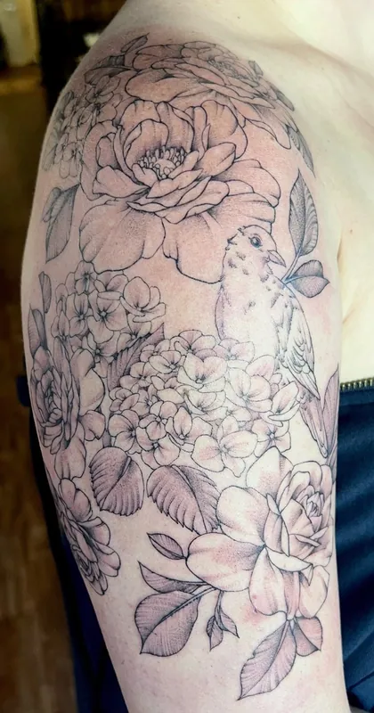 Black-and-grey fine-line half-sleeve tattoo of peonies, hydrangea and roses with a small perched bird on an upper arm