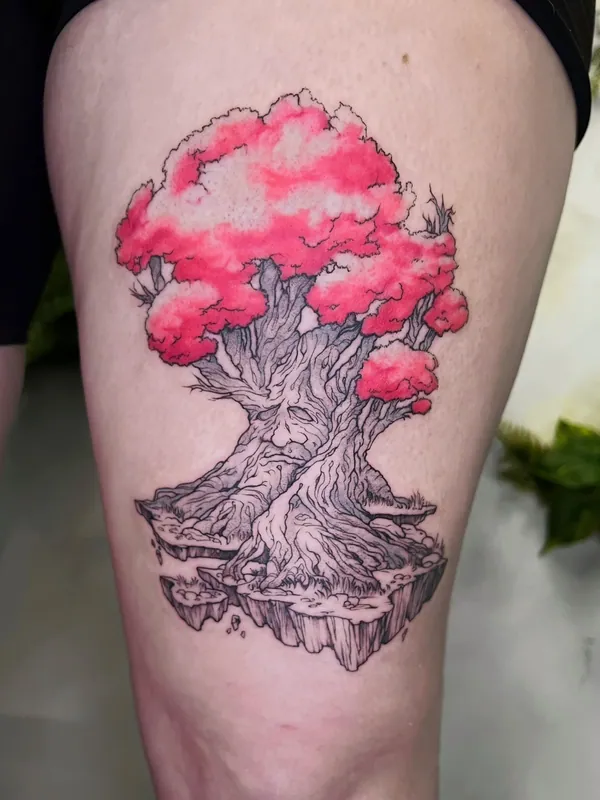 Tattoo of a gnarled tree with a pink color canopy growing on a floating island of rock and roots on a thigh