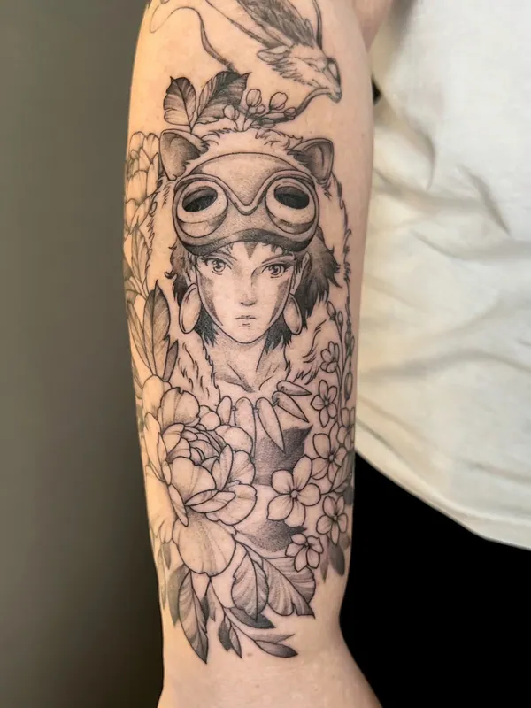 Black-and-grey tattoo of San from Princess Mononoke with her mask pushed up, a wolf above and peonies below, on an upper arm