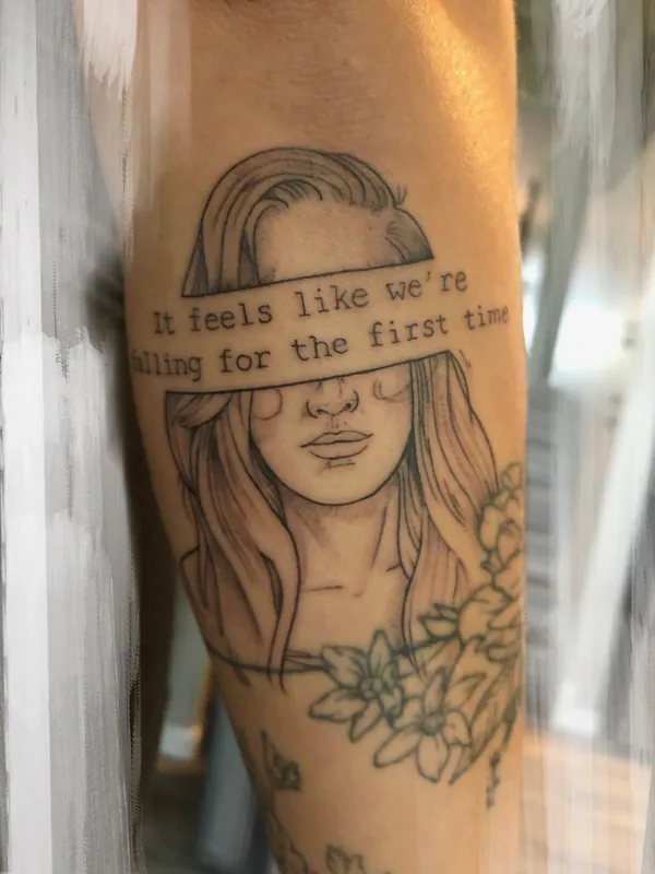 Fine-line black-and-grey tattoo of a woman whose eyes are covered by a band of typewriter text, with blossoms below, on a forearm