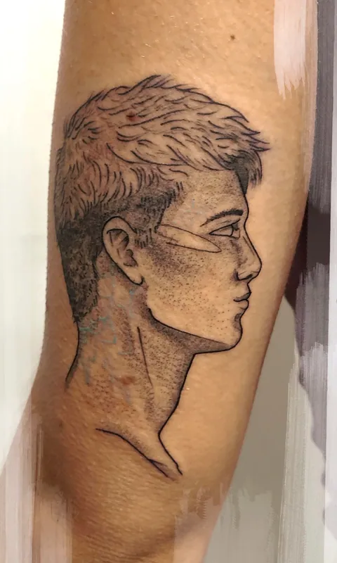 Black-and-grey dotwork profile portrait tattoo of a man with short textured hair on an inner upper arm
