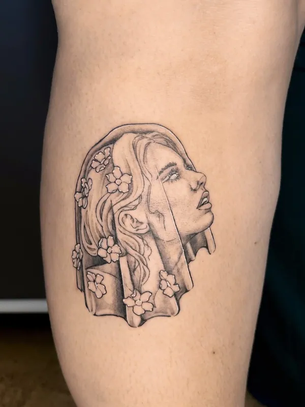 Fine-line black-and-grey tattoo of a woman in profile beneath a veil scattered with small blossoms on a calf
