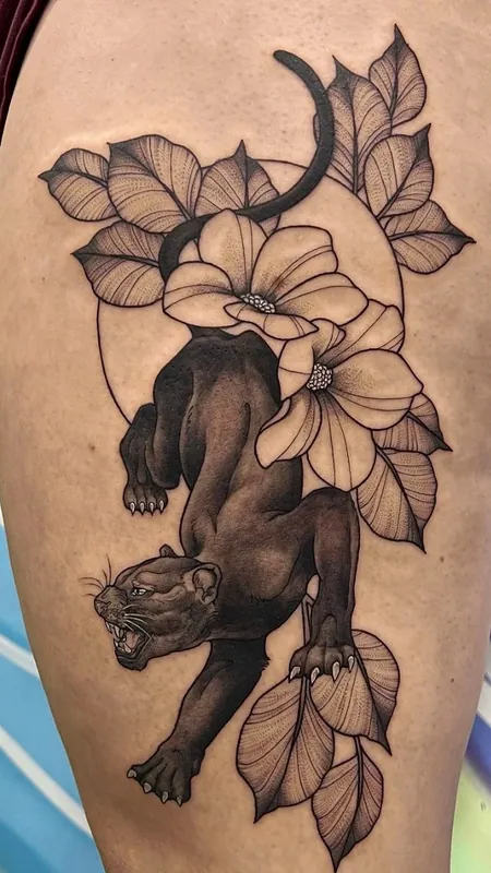 Black-and-grey tattoo of a prowling black panther beneath magnolia blooms and a thin circle on a thigh