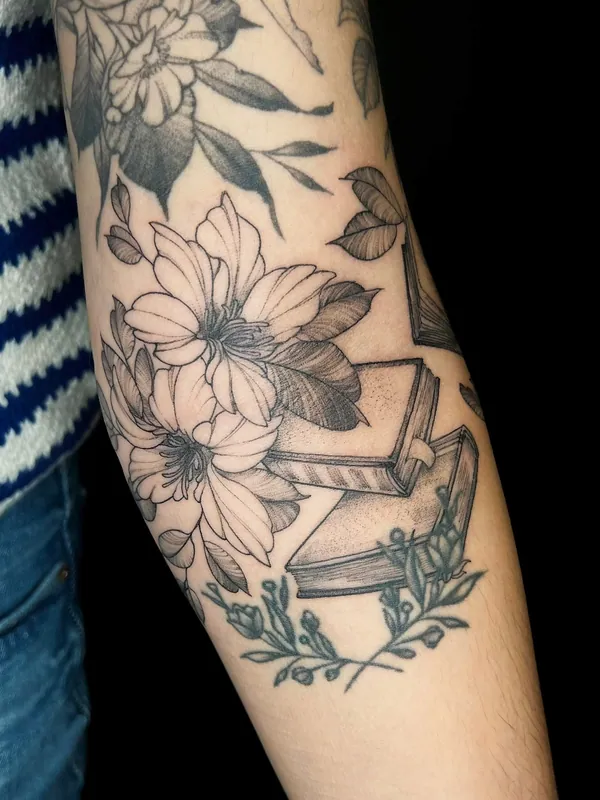 Black-and-grey fine-line tattoo of peony blooms over a stack of books on an inner forearm