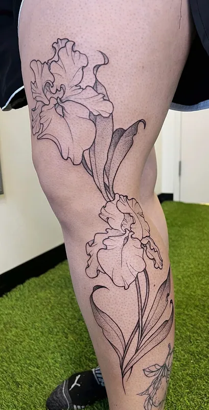 Black-and-grey dotwork iris tattoo running from the thigh down past the knee onto the calf