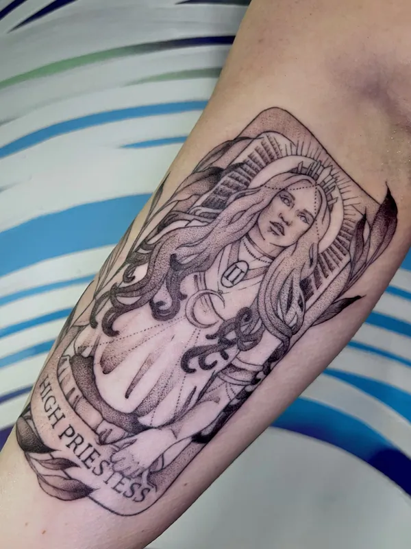 Dotwork black-and-grey tarot tattoo of the High Priestess with a crescent moon and crown, titled on a banner, on a forearm