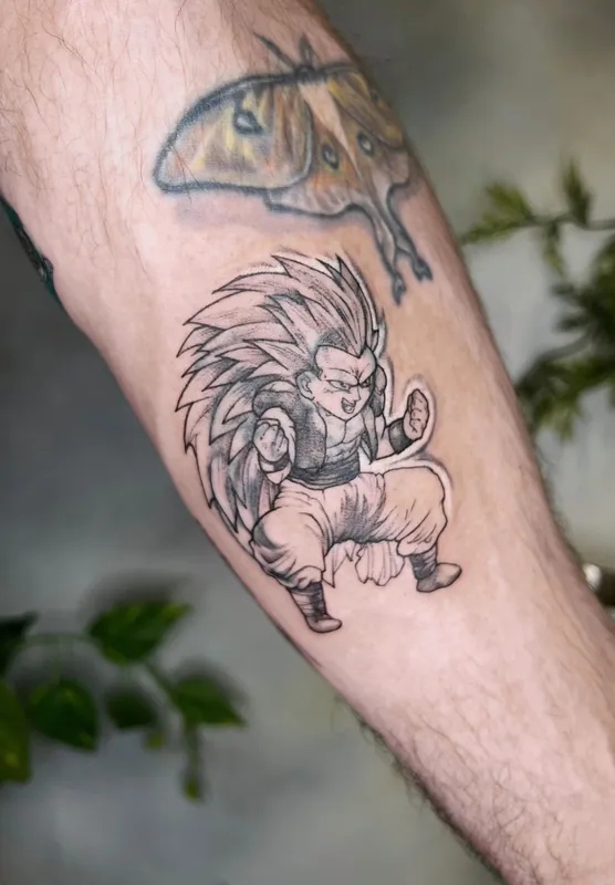 Black-and-grey anime tattoo of Gotenks in Super Saiyan 3 form, fists raised, on a forearm